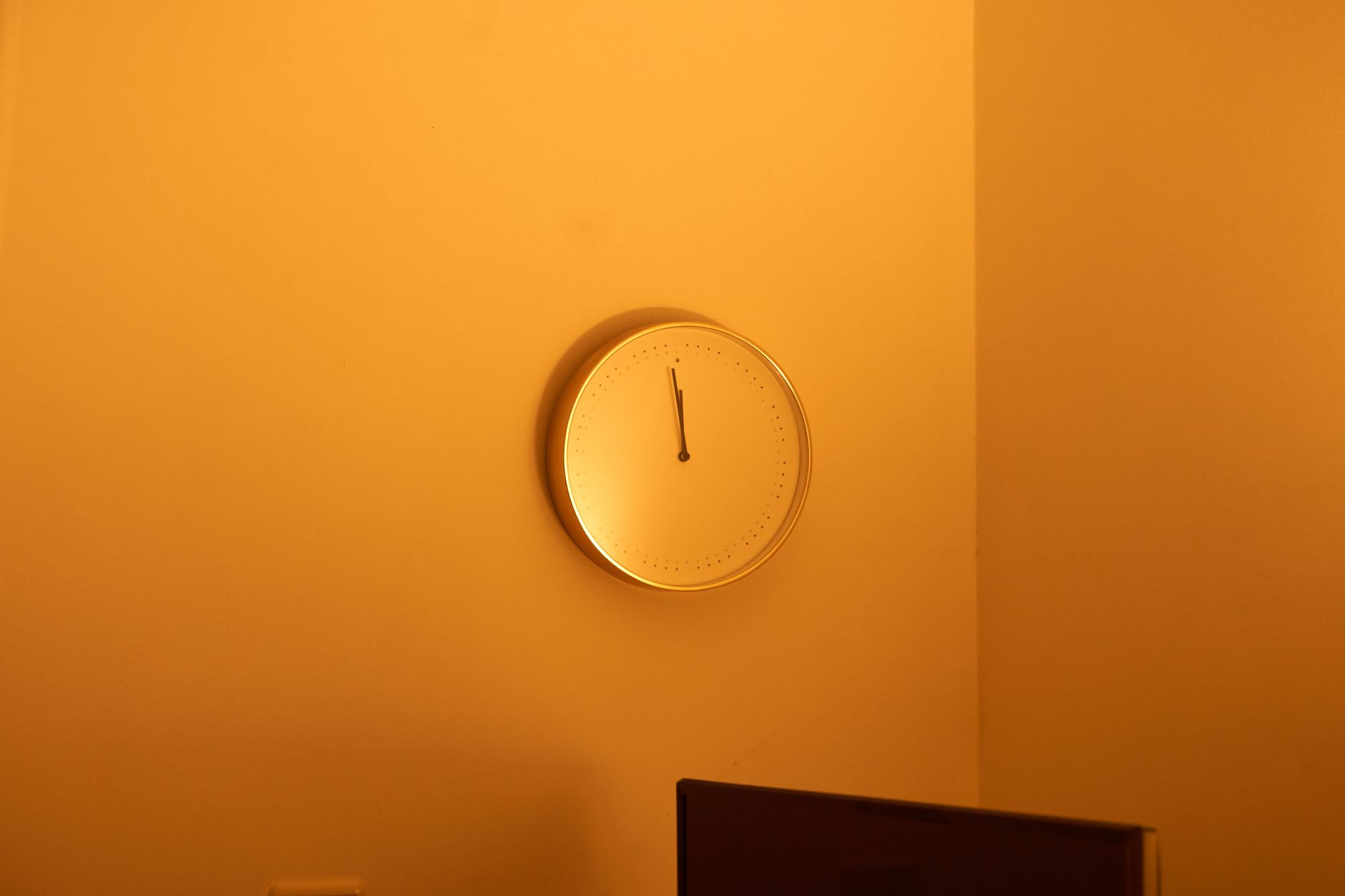 Um relógio de parede redondo e sem números, iluminado por luz quente numa parede lisa cor de âmbar.